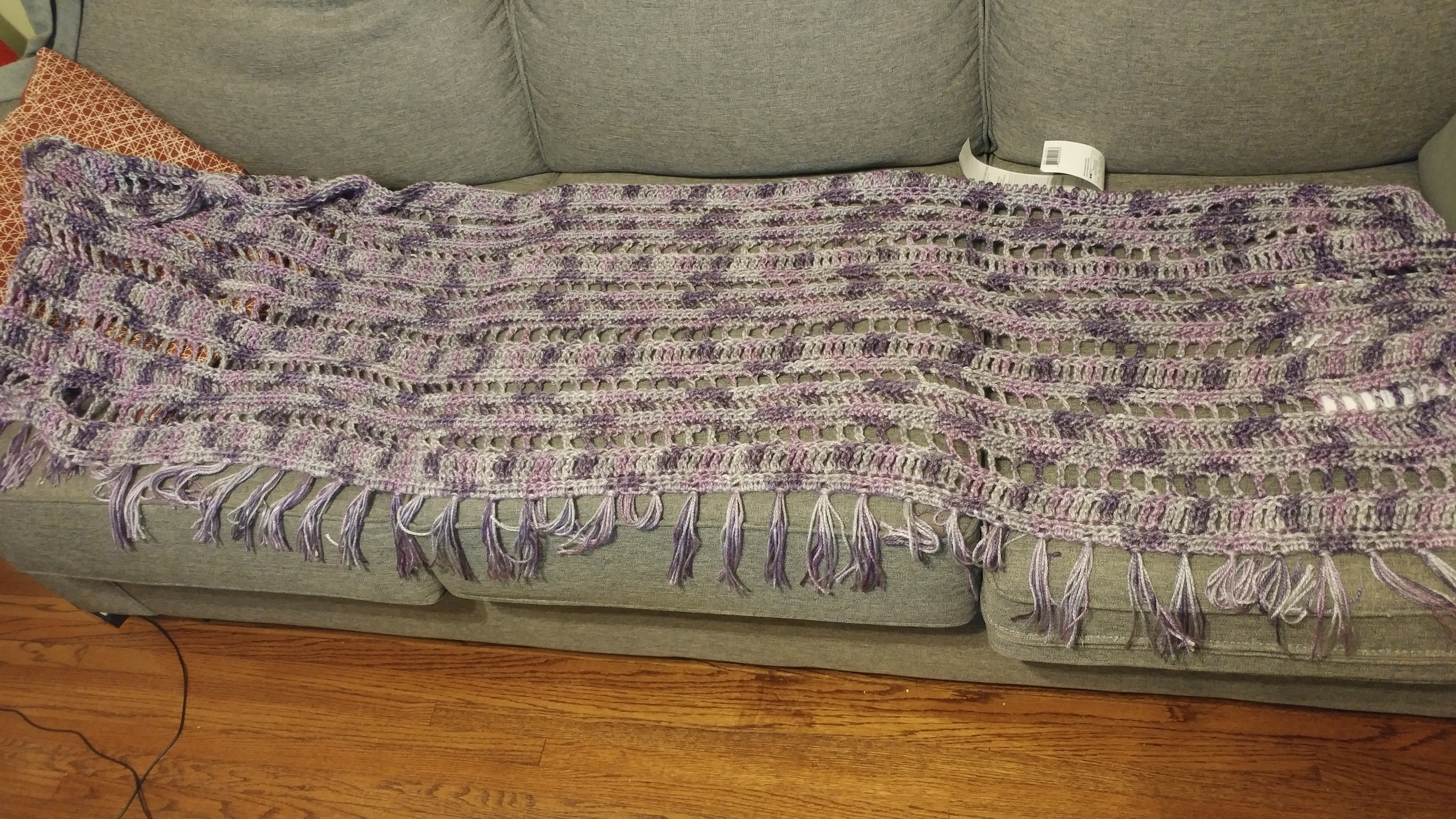 A rectangular shawl, crocheted in grey, pinkish-purple, and purple.
